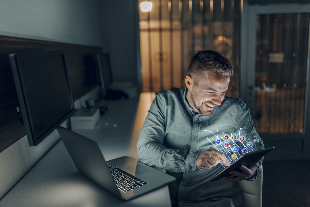 Marketing de Varejo: imagem mostra homem sentado de frente para computador, segurando e digitando em tablet. Ilustrações "saem" do tablet, indicando interatividade e tecnologia